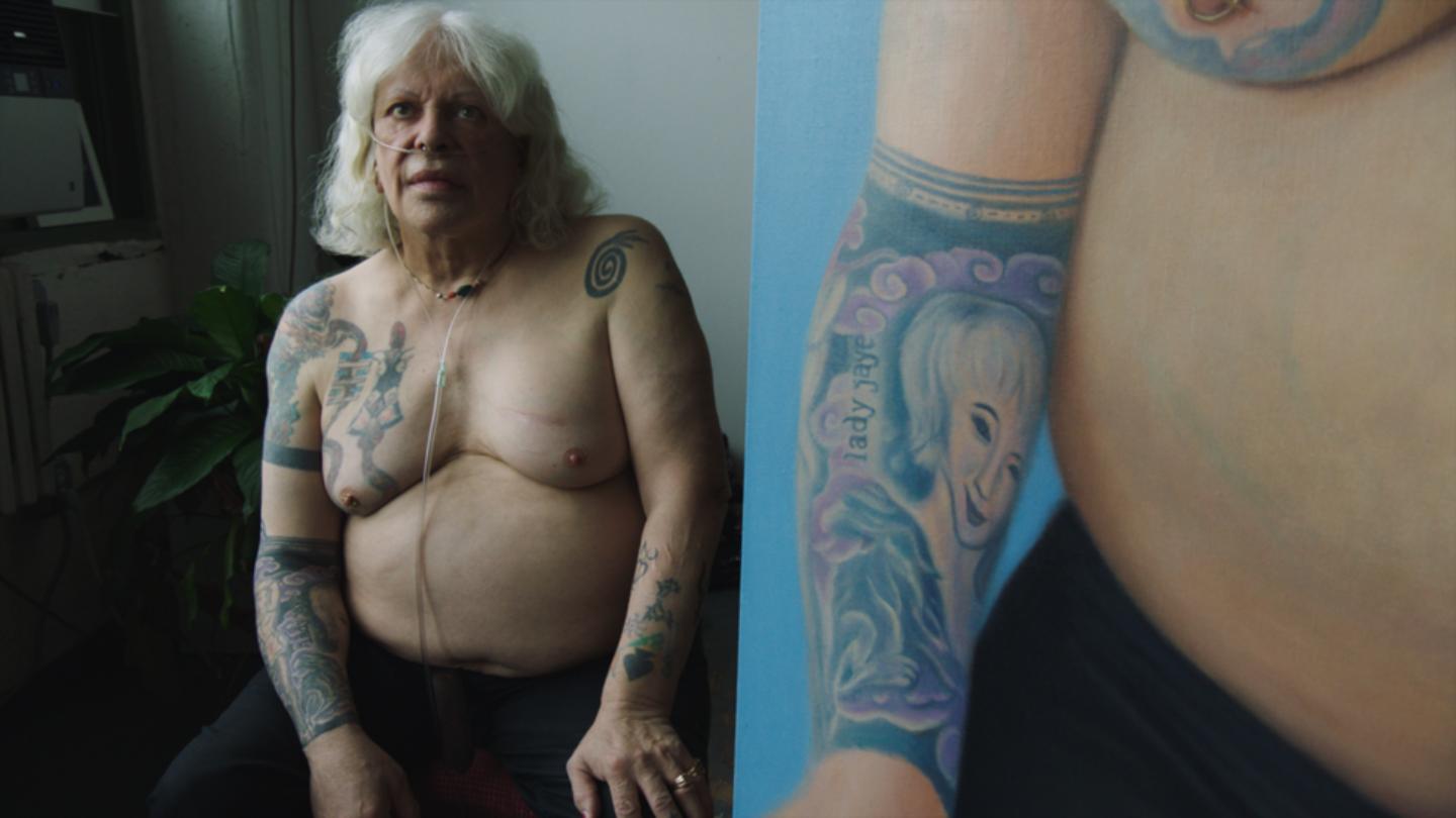 A split screen with someone shirtless, long blonde hair, tattoos & an oxygen tube running to the nose on the left and closeup of the right arm and tattoo of the same person on the right.