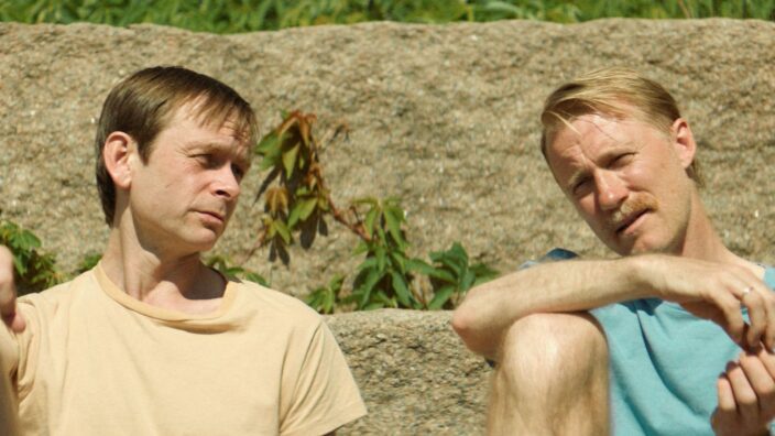 2 men sit side by side in a field