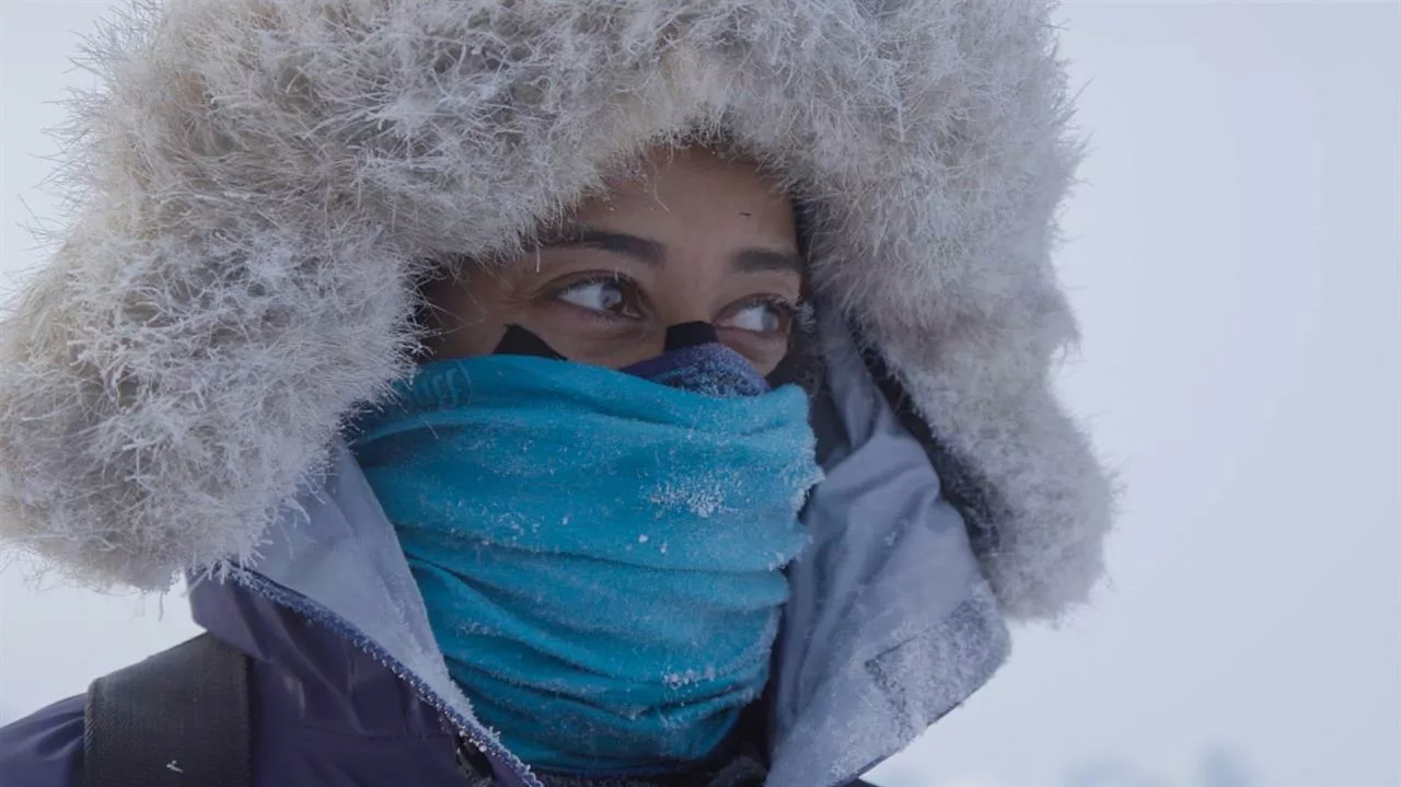 A person in a jacket that covers their face and head. Eyes looking to the distance. Background with white snow.