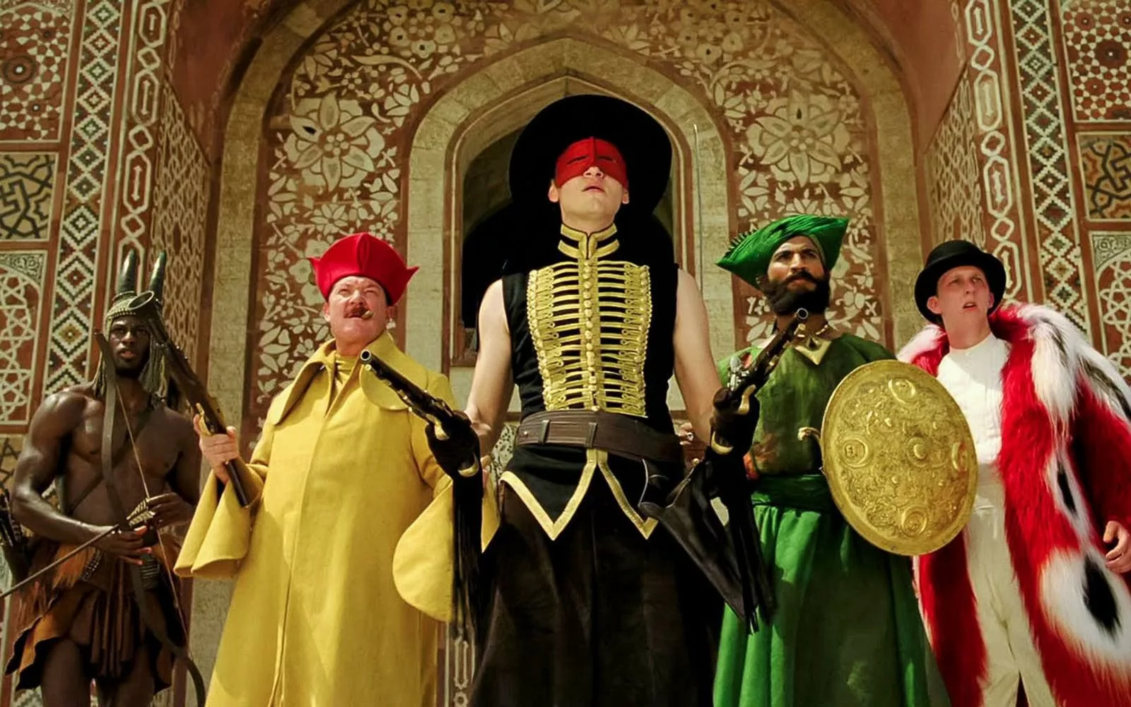 Five men, each holding a weapon, costumed so elaborately it's impossible to describe here, except the man in the center in a black, wide-brimmed hat and a black, gold-laced, sleeveless shirt, wearing a red mask across his eyes.