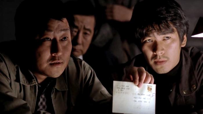 a man holds an stamped letter up high while another man stares besides him