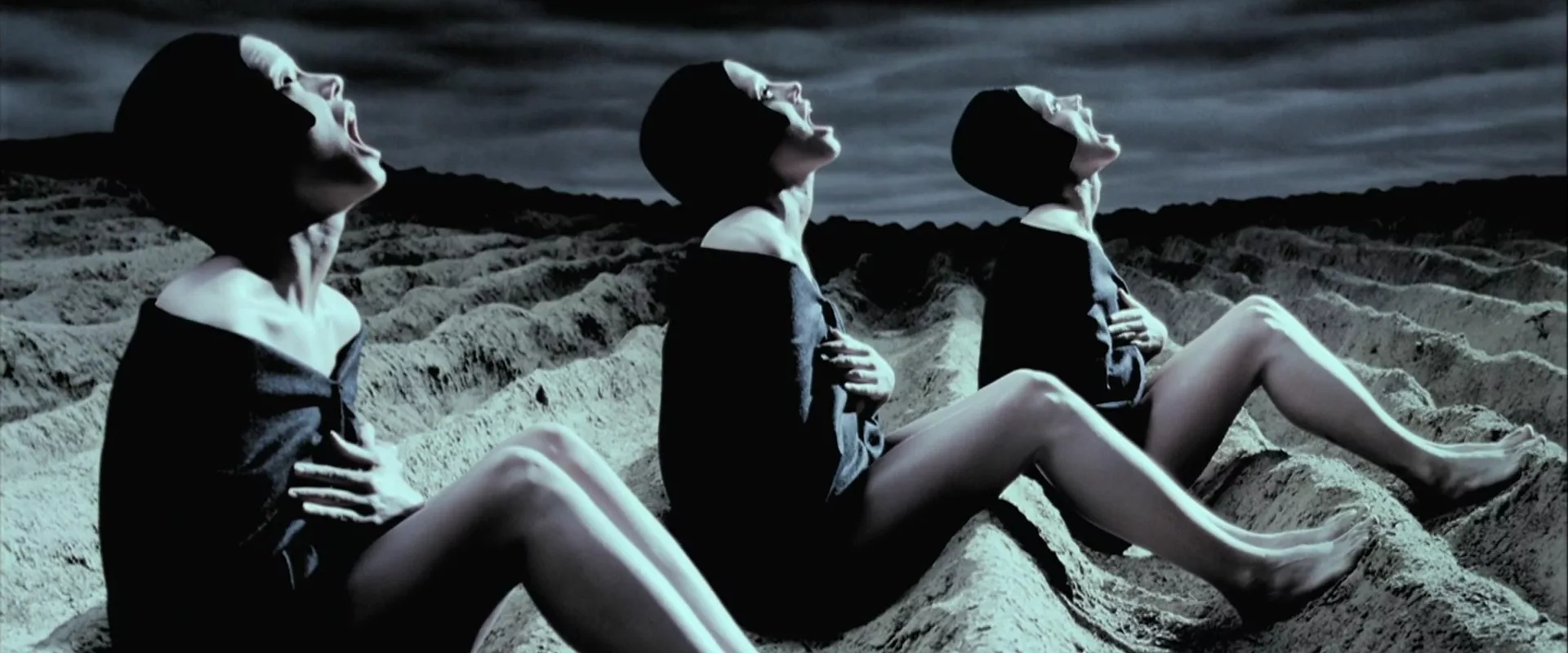 Three twin women screaming in the sky as they sit in sand dunes