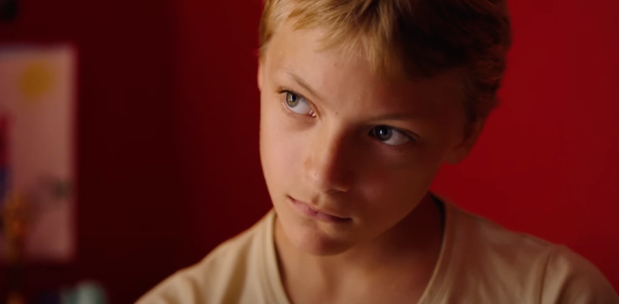 A little boy looking sideways as he sits against the red wall in Close, Oscar 2023 nominated international feature film