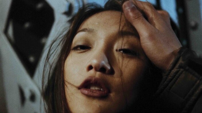 A young woman looking defiantly in the camera as a man pats her on the head