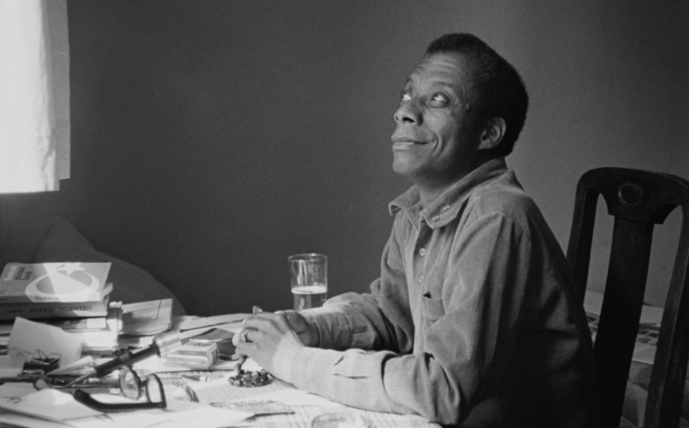 James Baldwin sitting at a desk full of papers