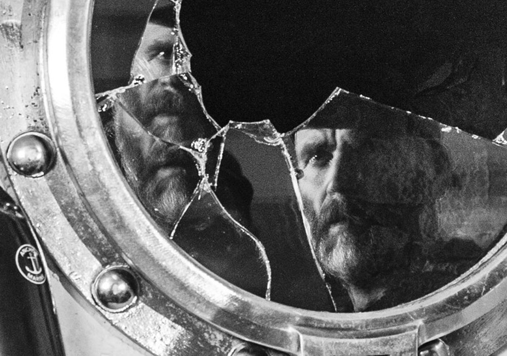A black-and-white bearded man in the broken mirror with parts of his face reflected crookedly in other pieces of the mirror