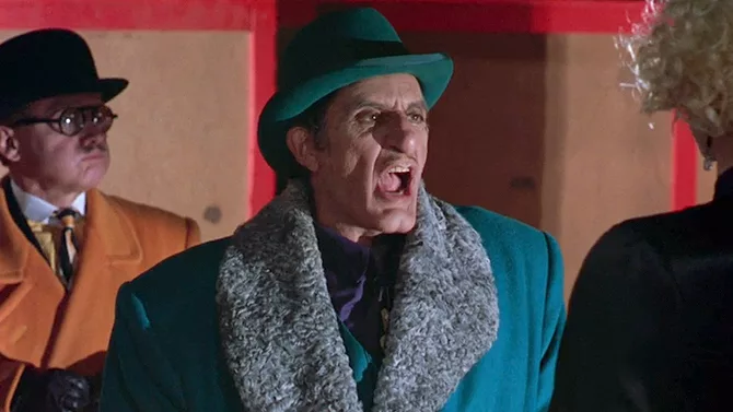 A scary man in an emerald hat and a furred collar jacket yelling at Madonna in an attempt to intimidate her, another spectacled man looking sideways behind them