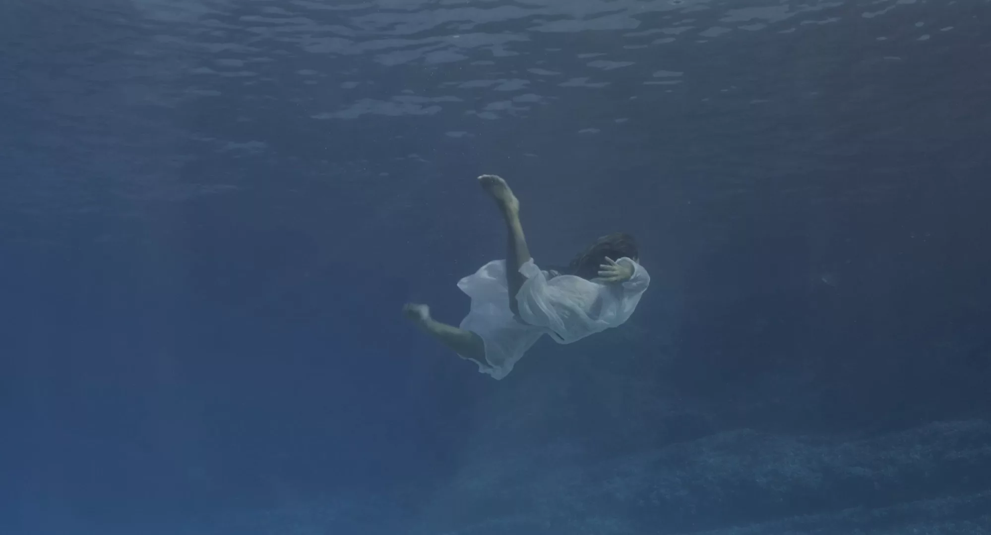 A person in a long white flowing dress is surrounded by blue water.