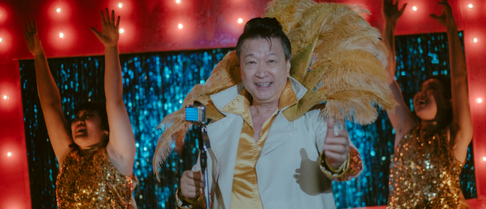 Asian man in a golden shirt and a white jacket performing on stage