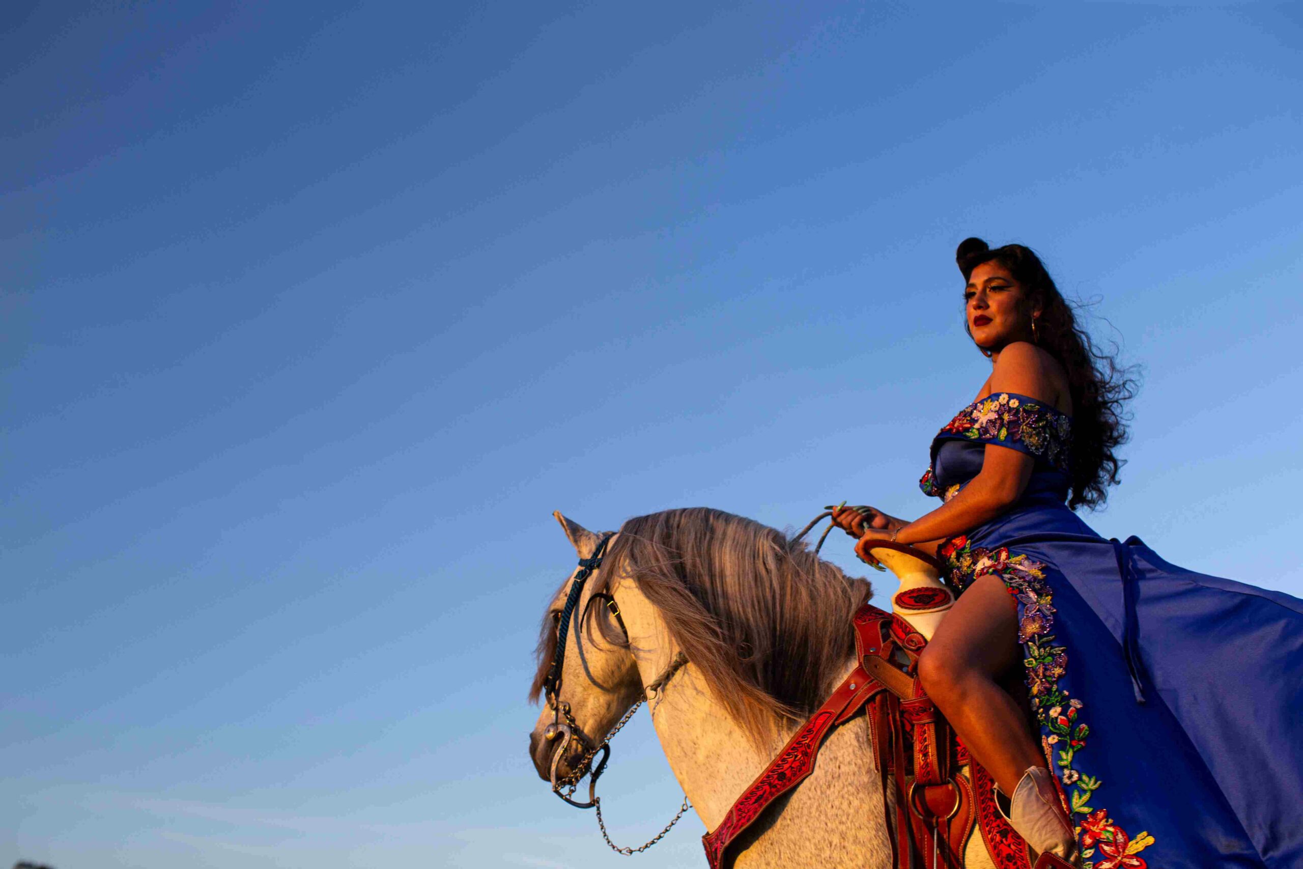 A woman in a dress on a horse with bright blue sky.