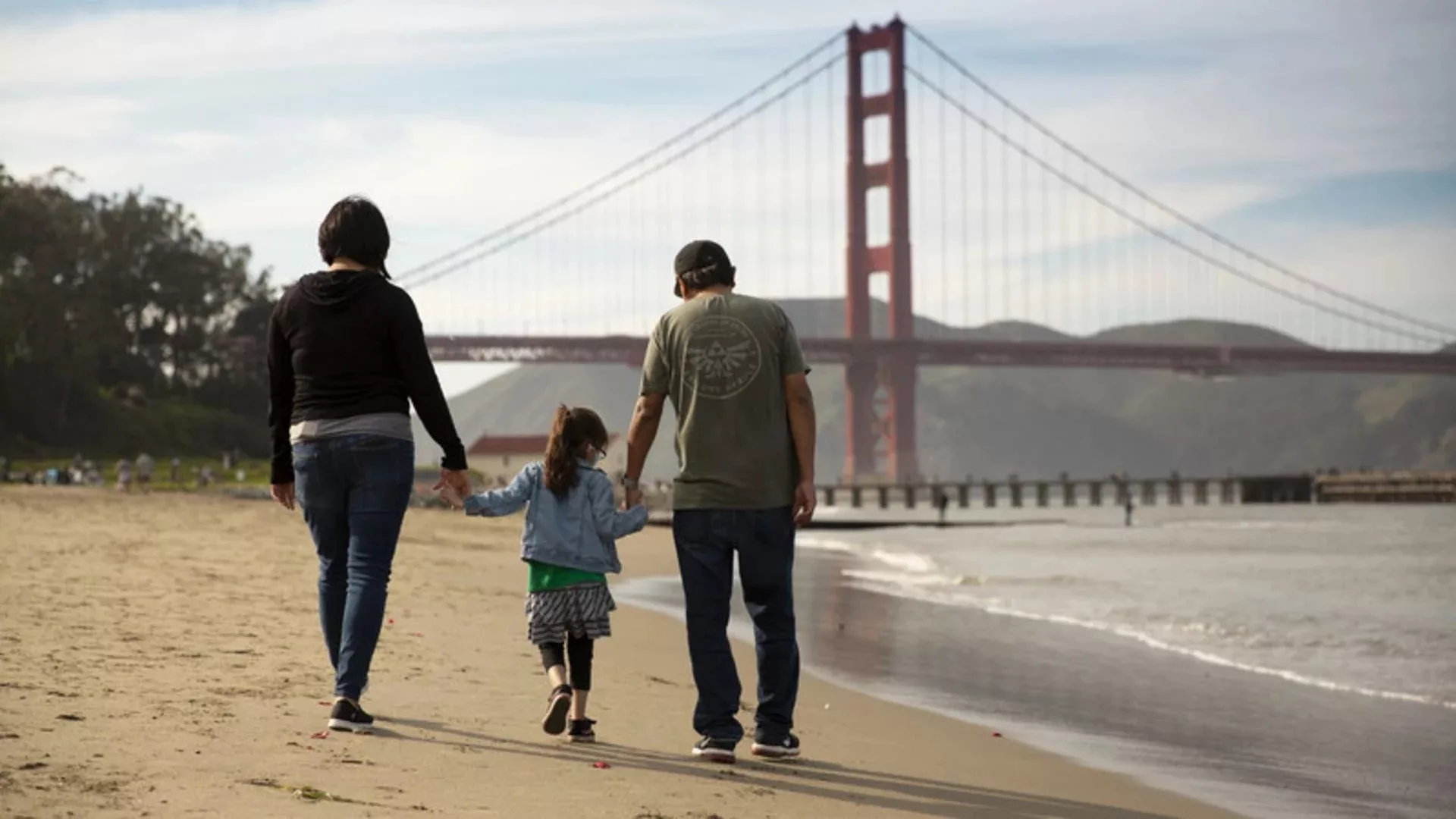 Family of three walk down the beach towards Golden Gate Bridge