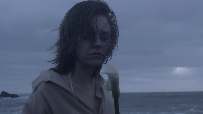 Sad young woman in a waterproof jacket by the sea