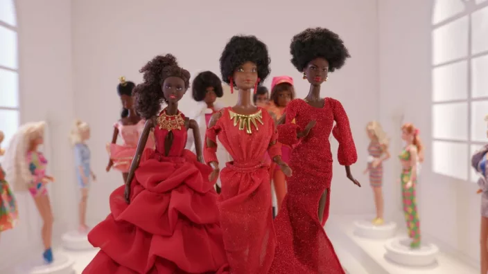 A lot of black barbie dolls standing in a circle in red ball dresses