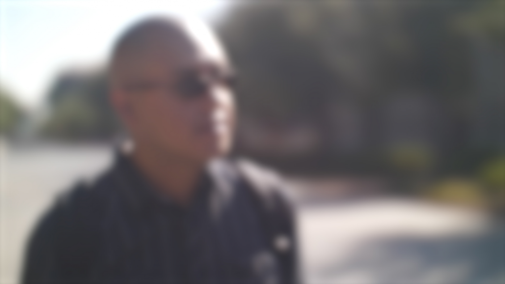 A bald man in sunglasses looking past the camera out of focus