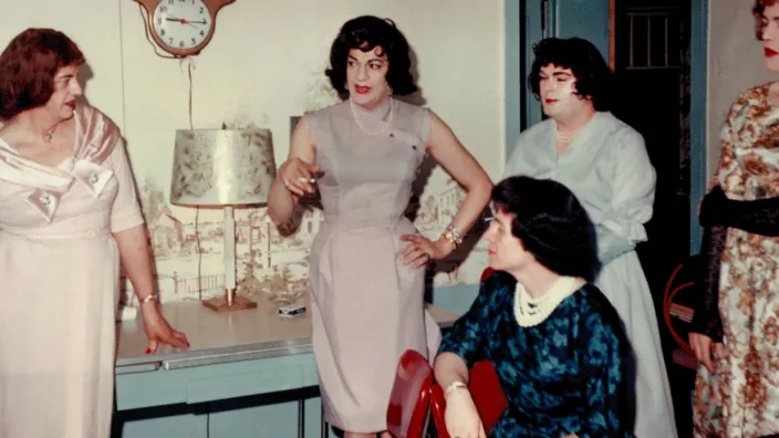 A group of trans women in festive gowns talk with one of them smoking a cigarette
