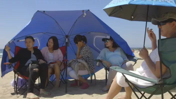 Chinese young women enjoying the weather as they sit on sandy beach under umbrellas