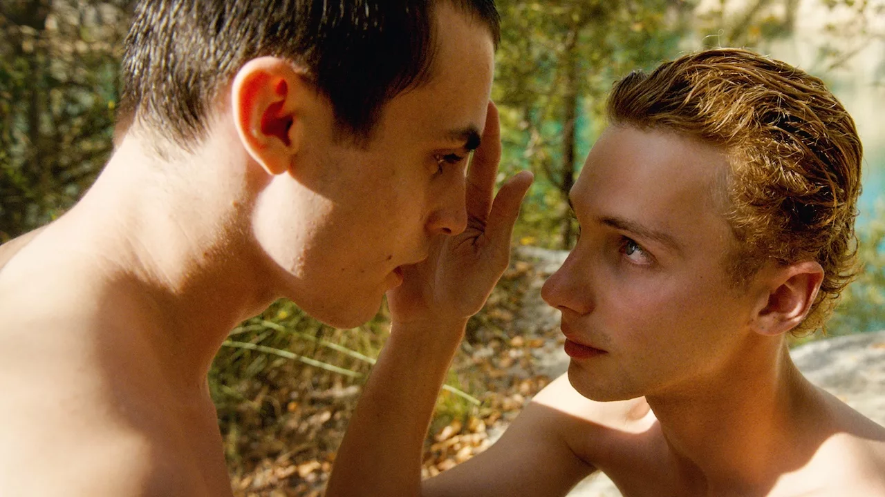 Young naked boy touching another boy's face with his hand as they look each other in the eyes