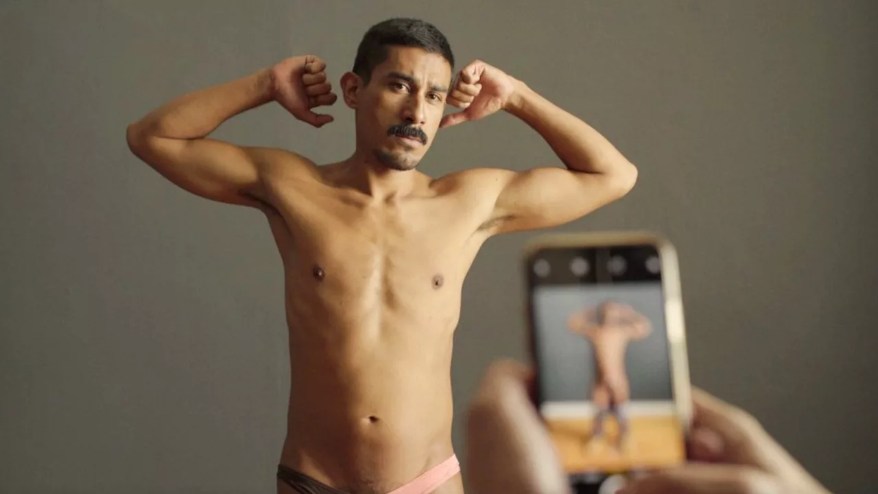 A half-naked guy flexes his biceps as he poses in front of someone taking pictures of him on the phone