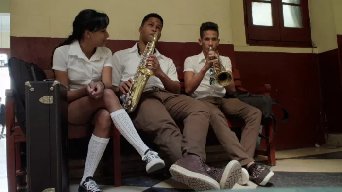 MVFF46: MÚSICA! - A girl and two boy sitting together as the boys play saxophone and horn instrument.