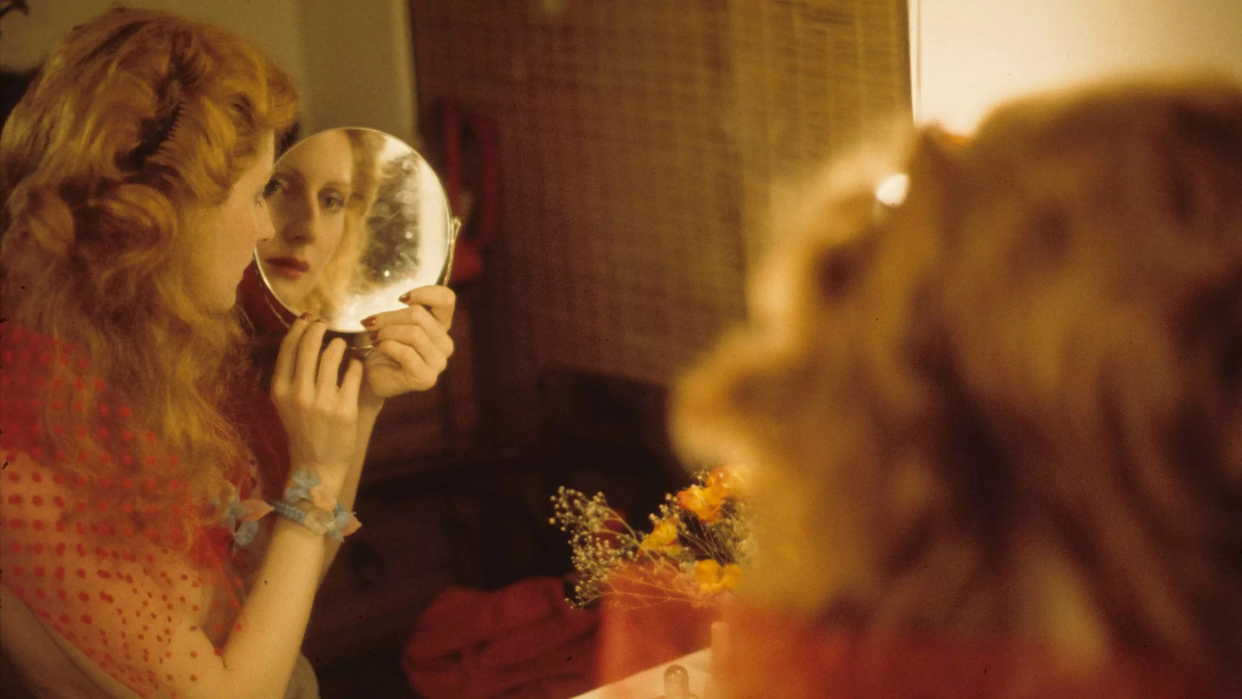 A woman with red hair looks at her own reflection from several mirrors.