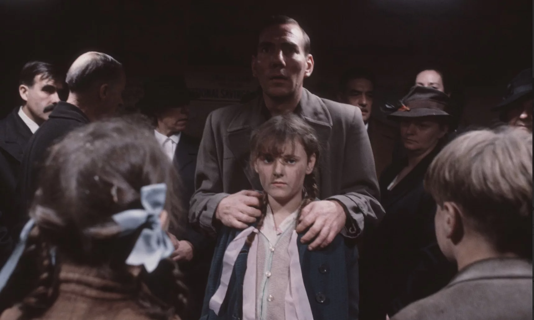 A man with a shocked look on his face stand behinds and holds a young girl amidst a crowd of people