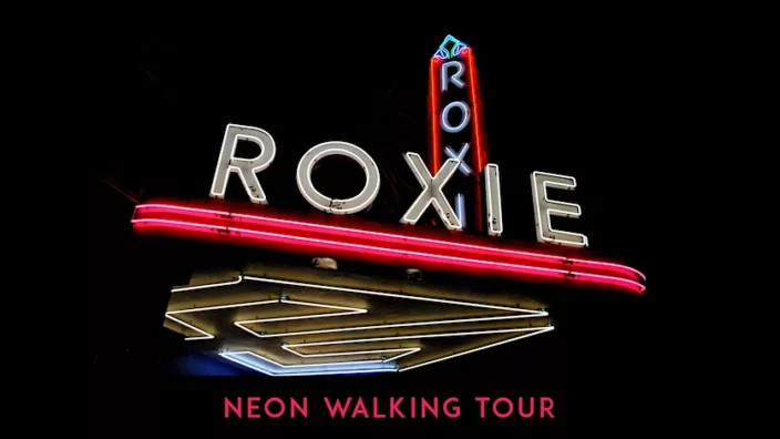 Glowing neon of Roxie marquee lit up with a dark night sky in the bathroom. Text at the bottom says neon walking tour - in bright pink letters.