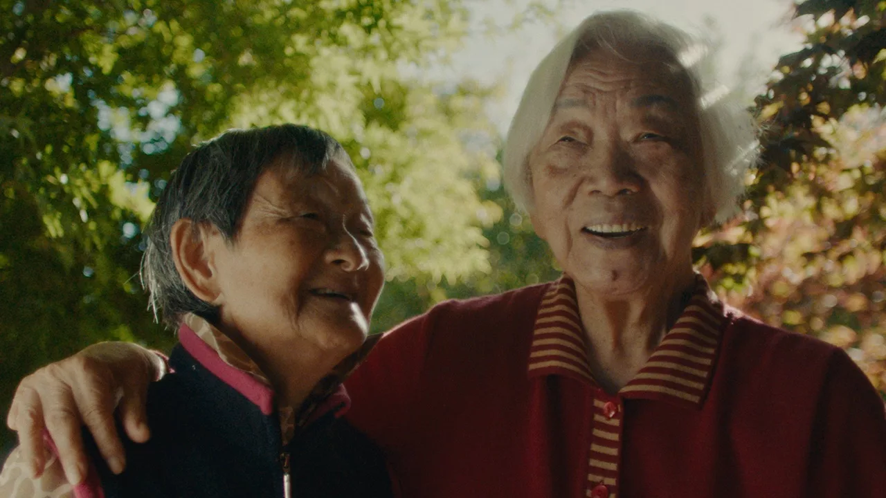 2 elderly Asian women smile as one holds the other around the shoulder