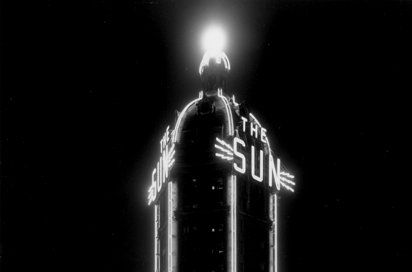 Black and white image with neon glowing white sign outlining The Sun sign.