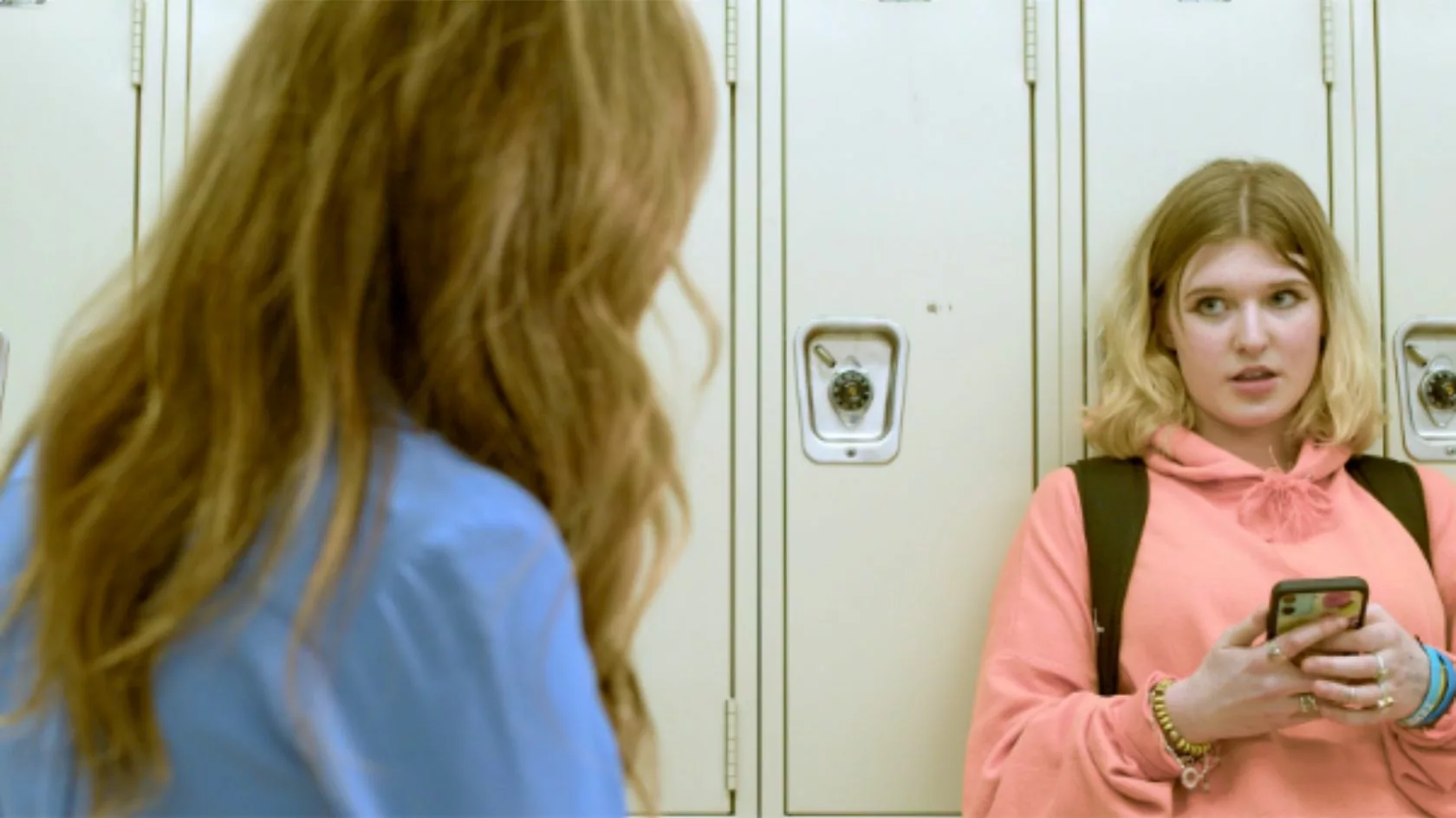 Woman talking to girl standing against locker.