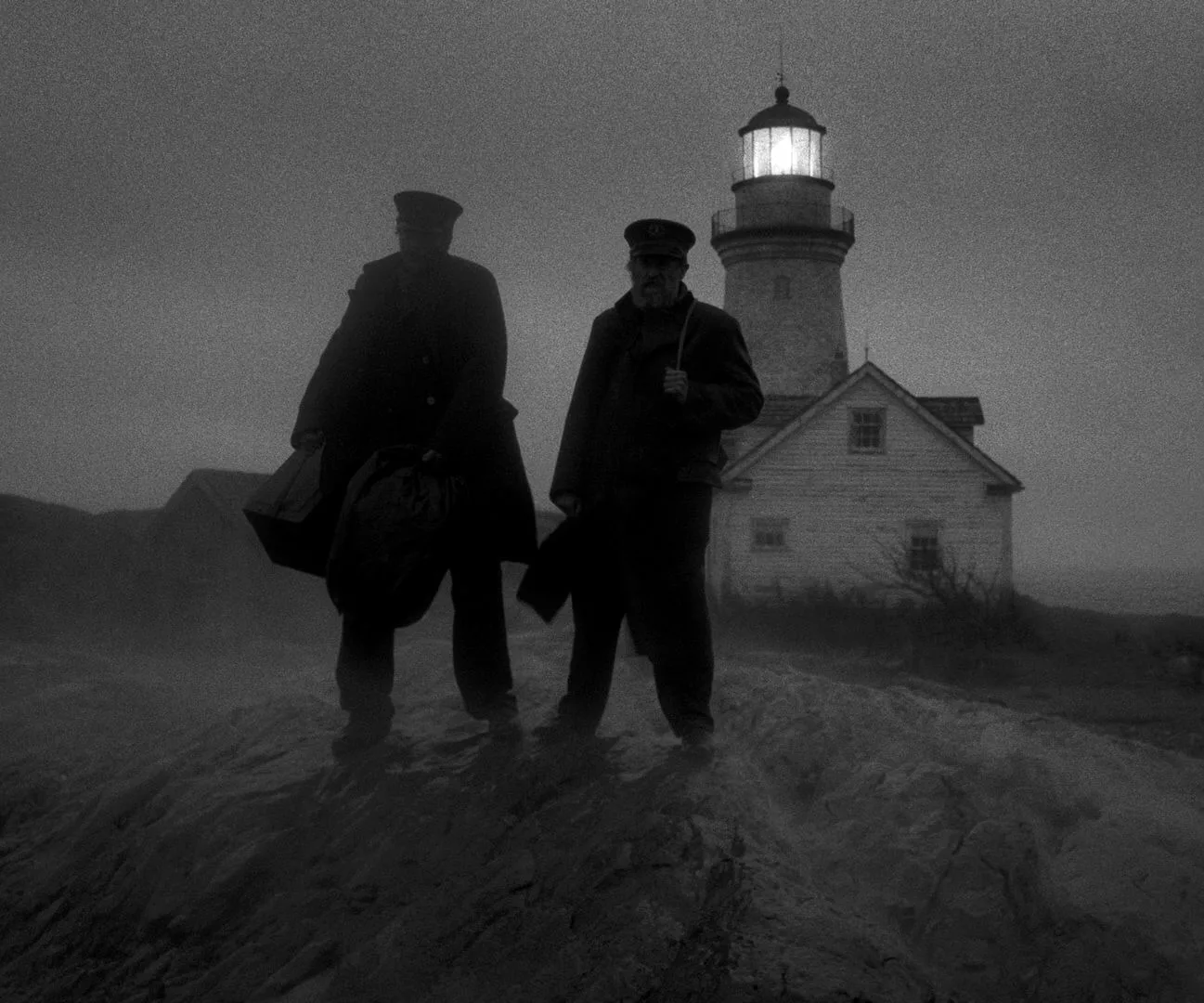 Silhouette of two men standing at the edge of a seaside cliff with a lighthouse glowing behind them