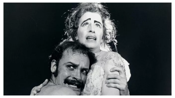 A man with mustache clutches a woman with an expression of dismay