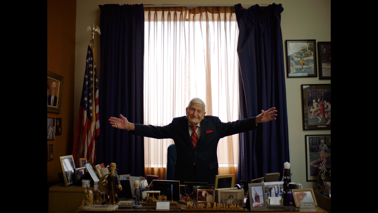 Senior attorney looks at audiences with arms open in his office