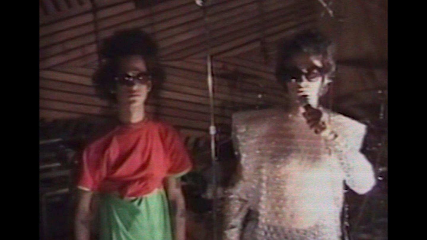 Two men stare at camera with glasses on, one holds microphone